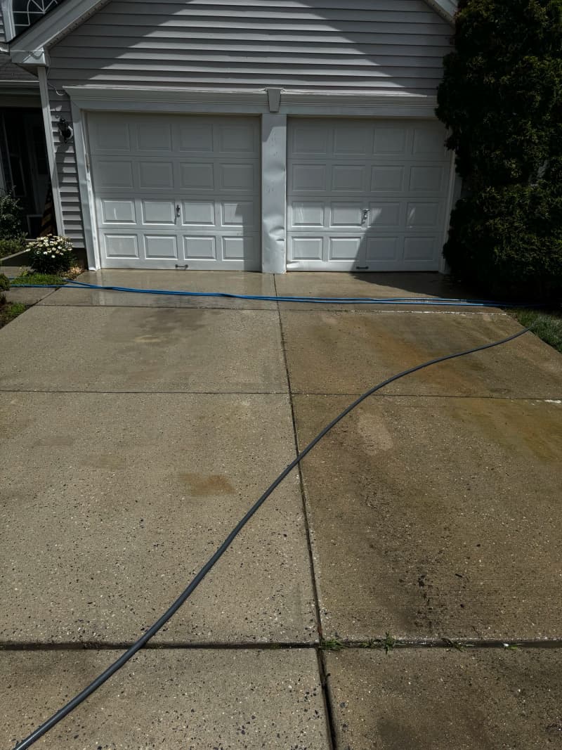 A two-car driveway in front of a garage, partway through a pressure wash
