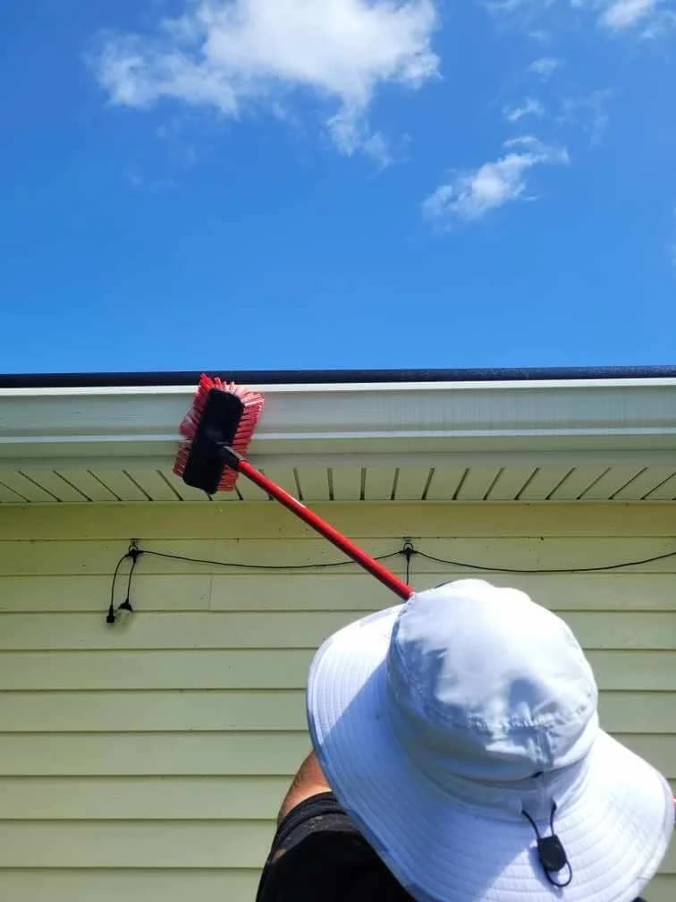 Scrubbing the face of a white gutter with a brush on a pole